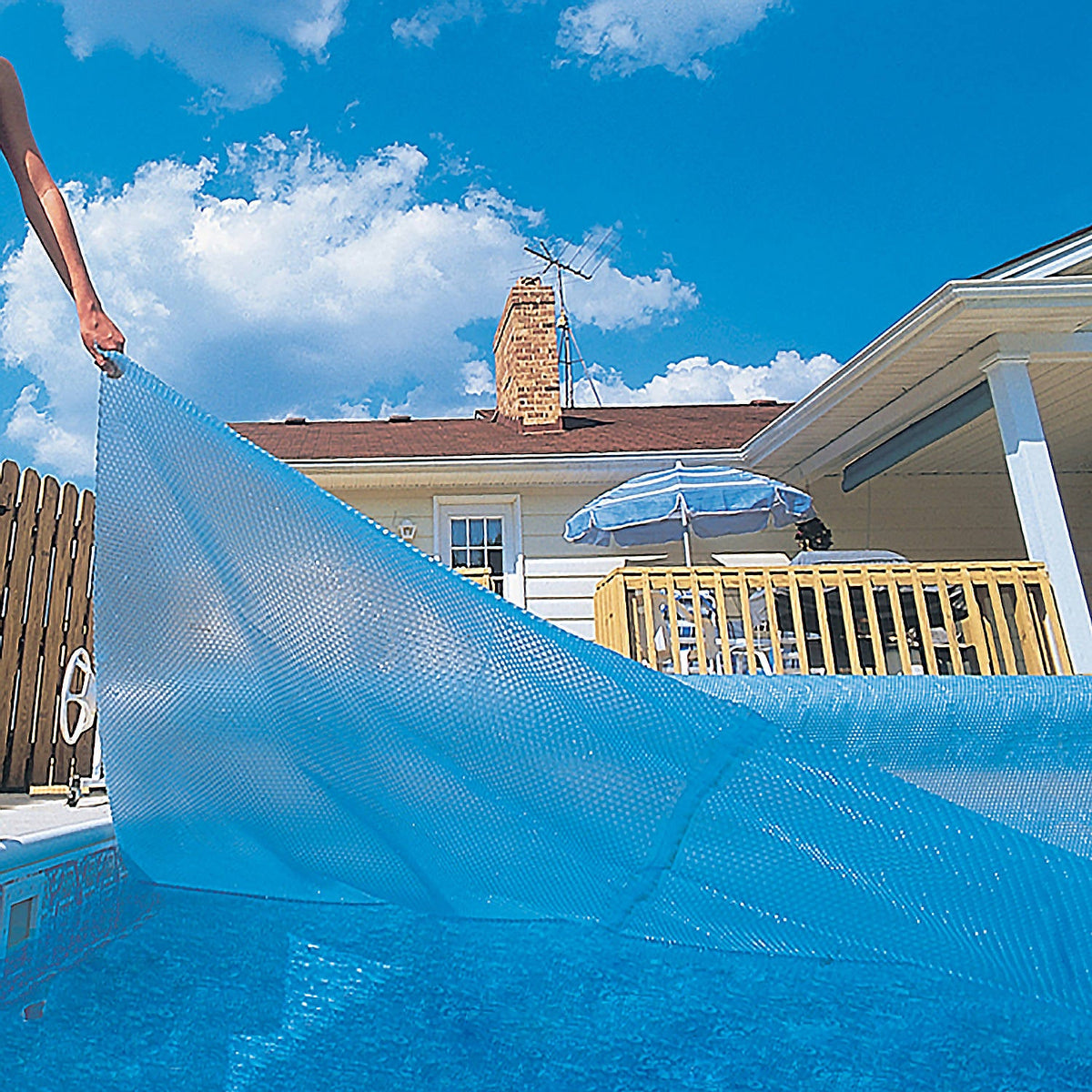 Blue Wave 12-mil Rectangular Solar Blanket - blanket being drawn across an in-ground pool by hand