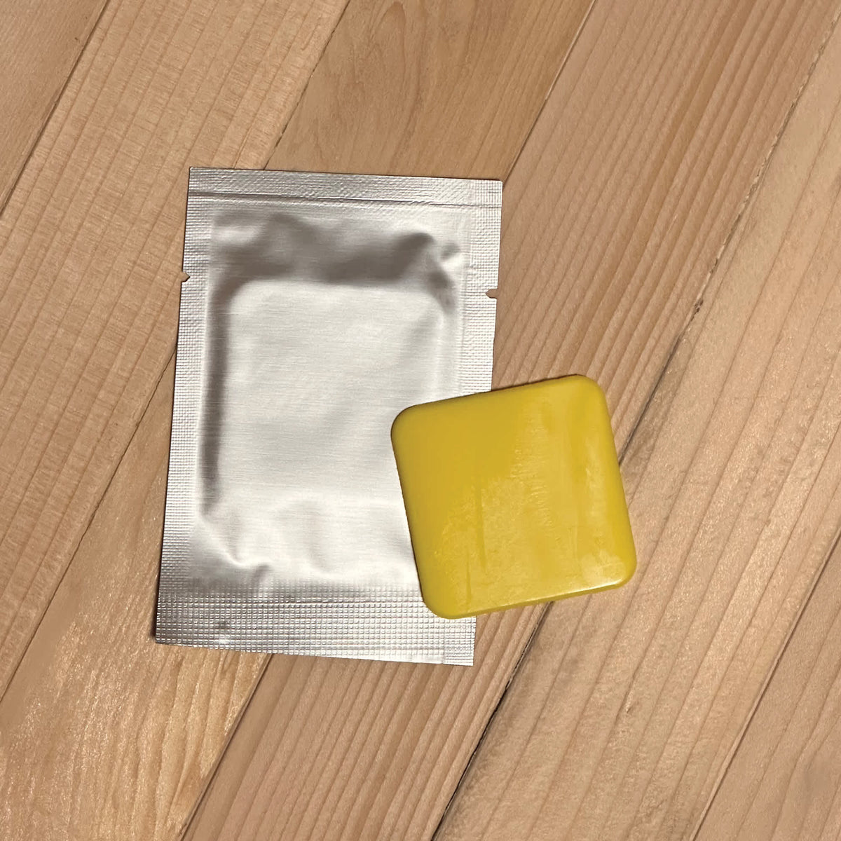HeatWave Sauna Fragrance Pad - single pad beside its sealed foil sachet on sauna decking